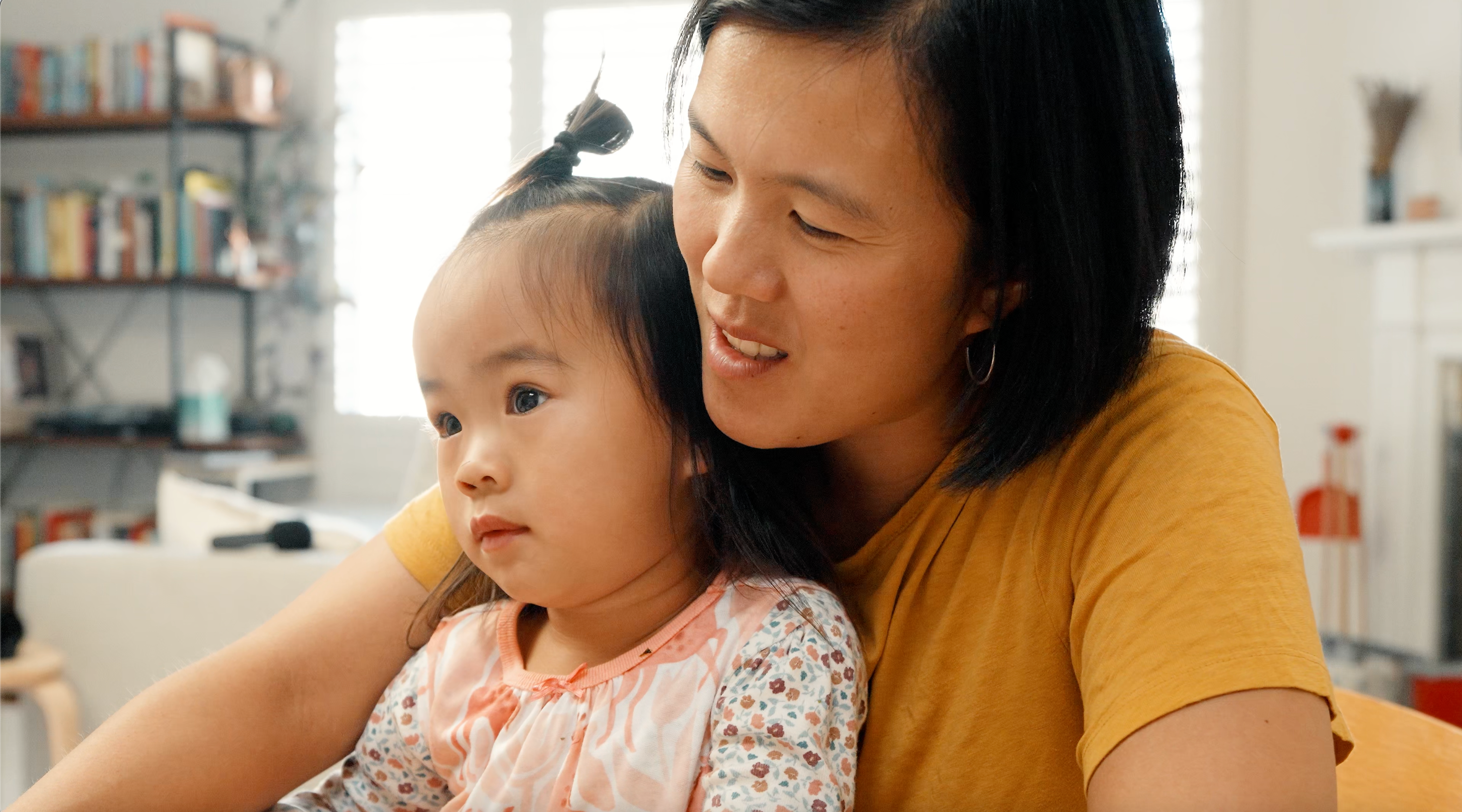 Woman wearing a yellow t-shirt with short black hair and a toddler on her lap