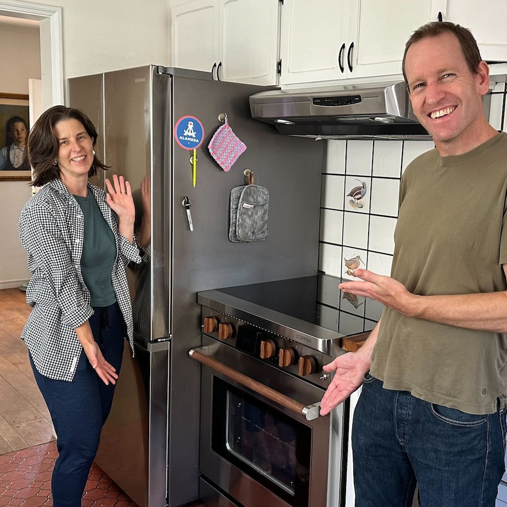 A man and woman stand in their kitchen proudly showing off their Copper Charlie battery-equipped 120v compatible induction range.