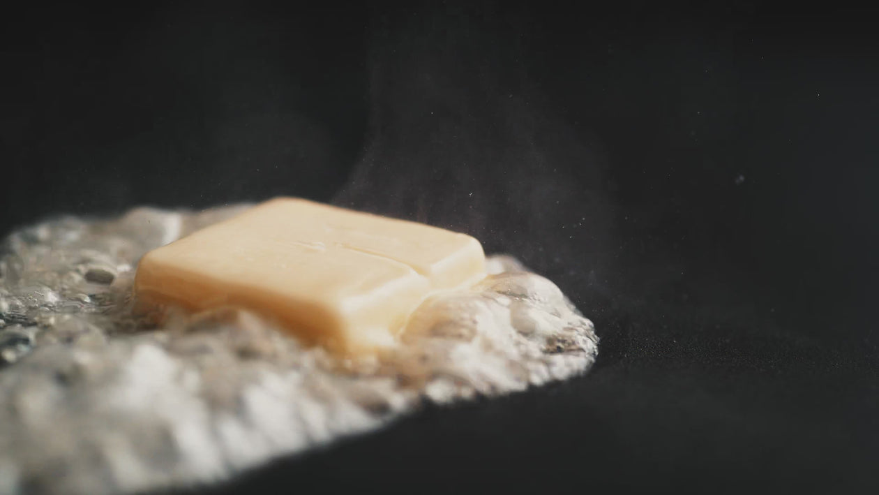 Close-up shot of butter melting in a pan that transitions into a shot of a seared steak with a sprig of thyme being placed on top. 