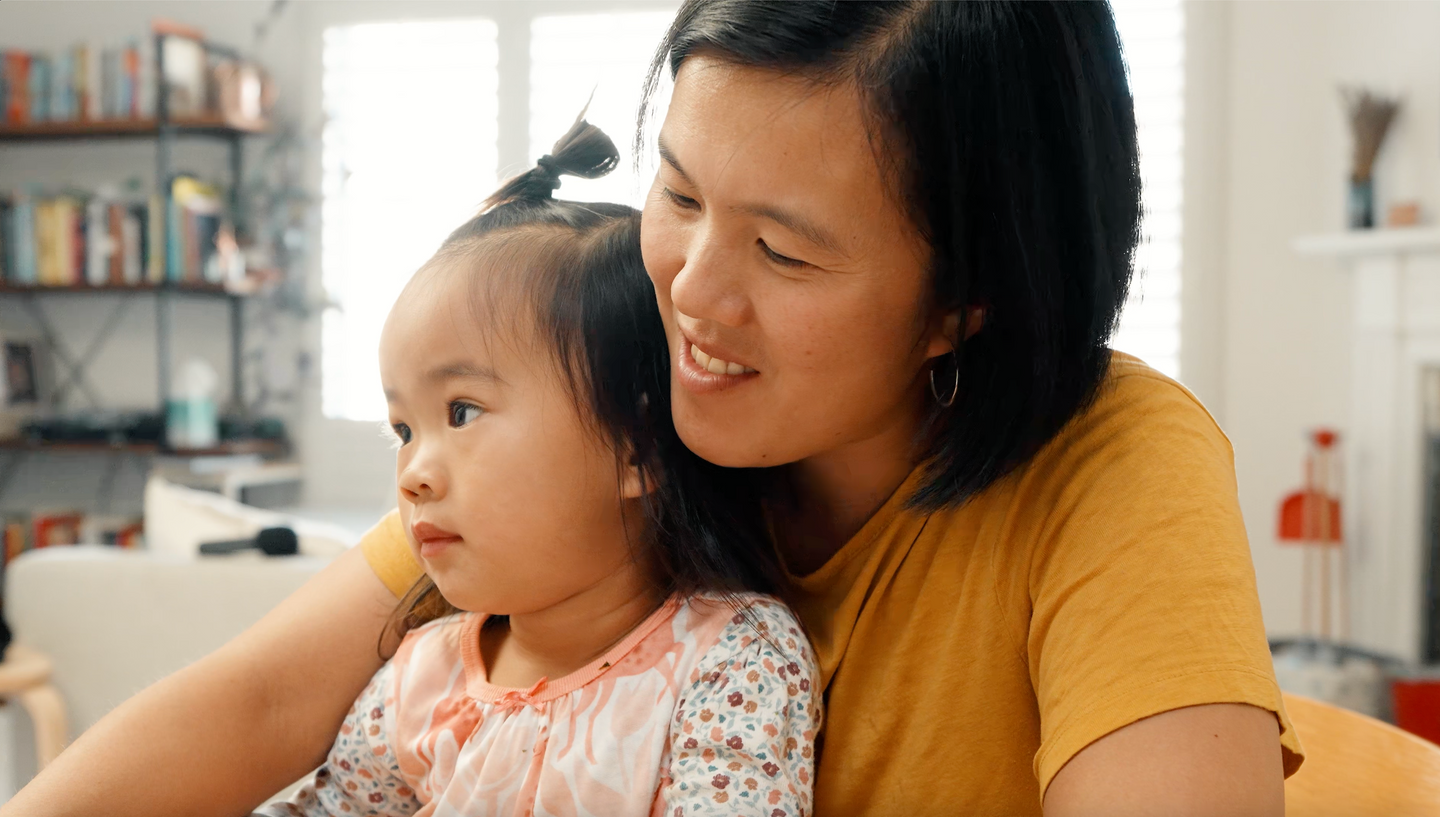 Woman wearing a yellow t-shirt with short black hair and a toddler on her lap 